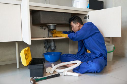 asian plumber blue overalls clearing blockage drain 